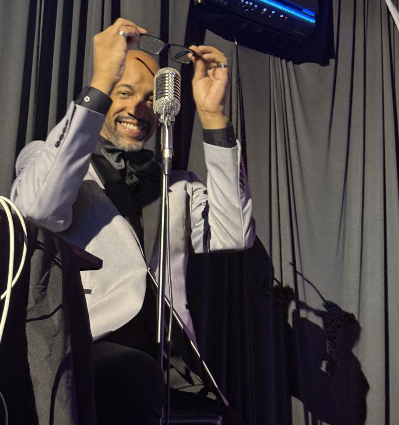 Antonio laughing as he adjusts his glasses at the mic